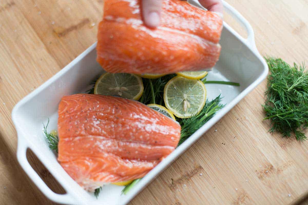 Placing salmon on top of lemon slices, fresh dill, and add a little liquid.