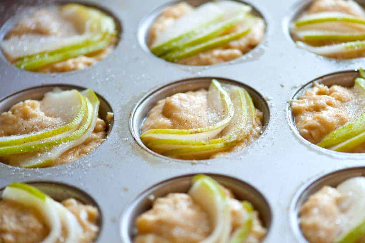 Unbaked pear muffin batter in a muffin tin with fresh pear slices pressed into the tops.