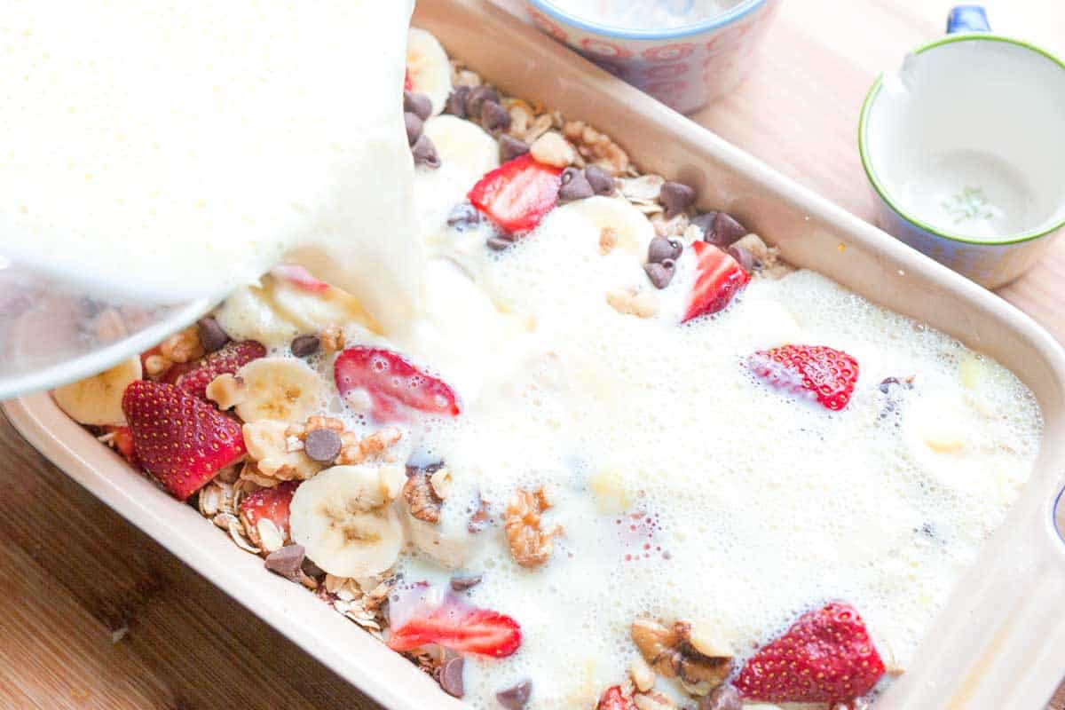 Pouring the milk mixture into a baking dish with oats, sugar, and fruit.