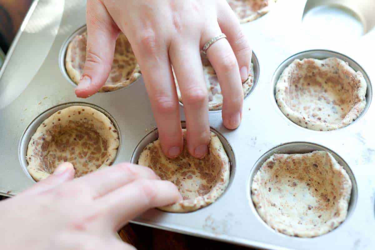 Pressing the cinnamon roll crust into cupcake tin
