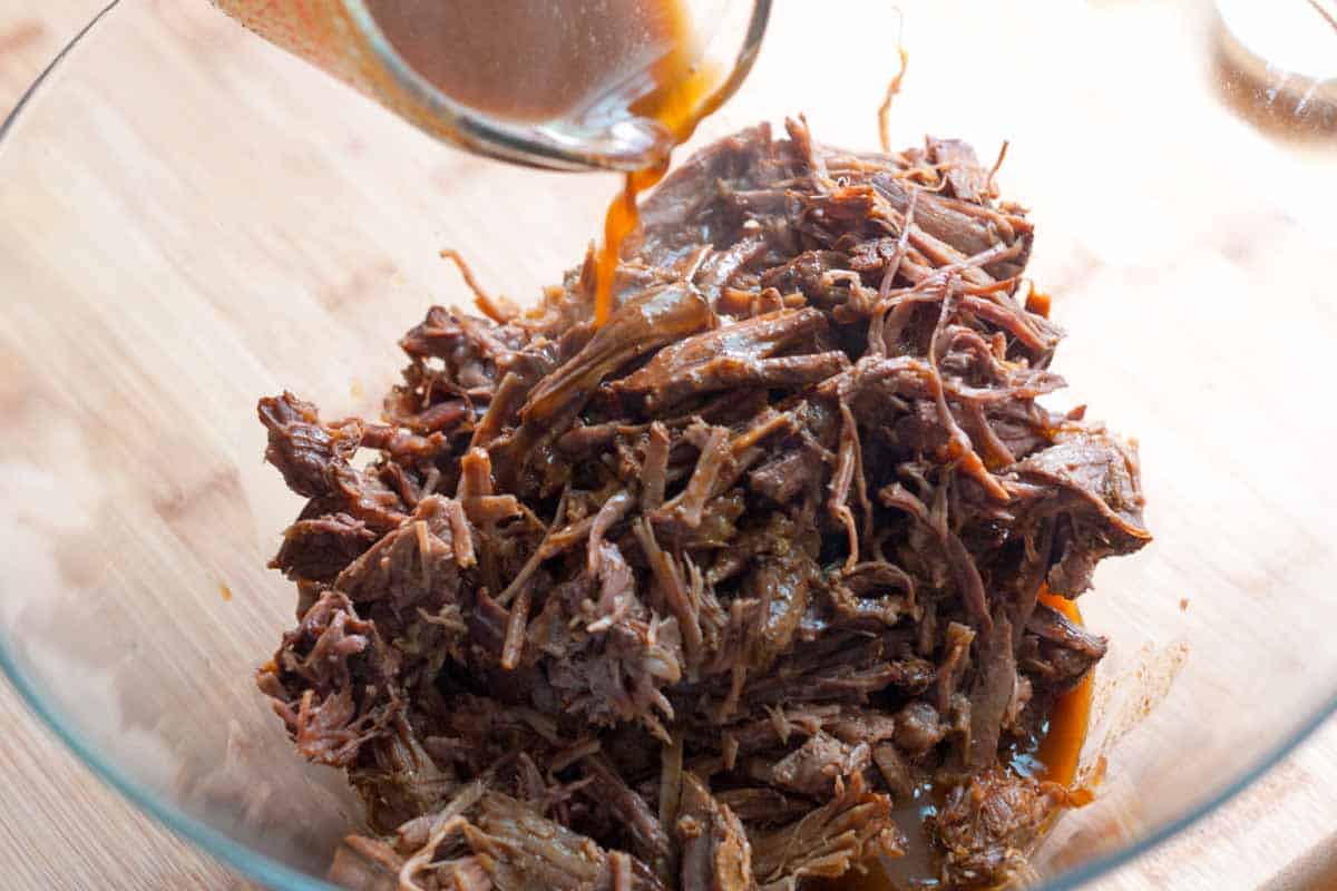 How to Make Irresistible Shredded Beef Tacos Pouring cooking liquid over shredded beef before building tacos