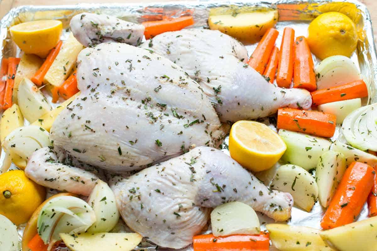 Rosemary Roasted Butterflied Chicken with Vegetables Spatchcock chicken on a baking sheet with vegetables and lemons