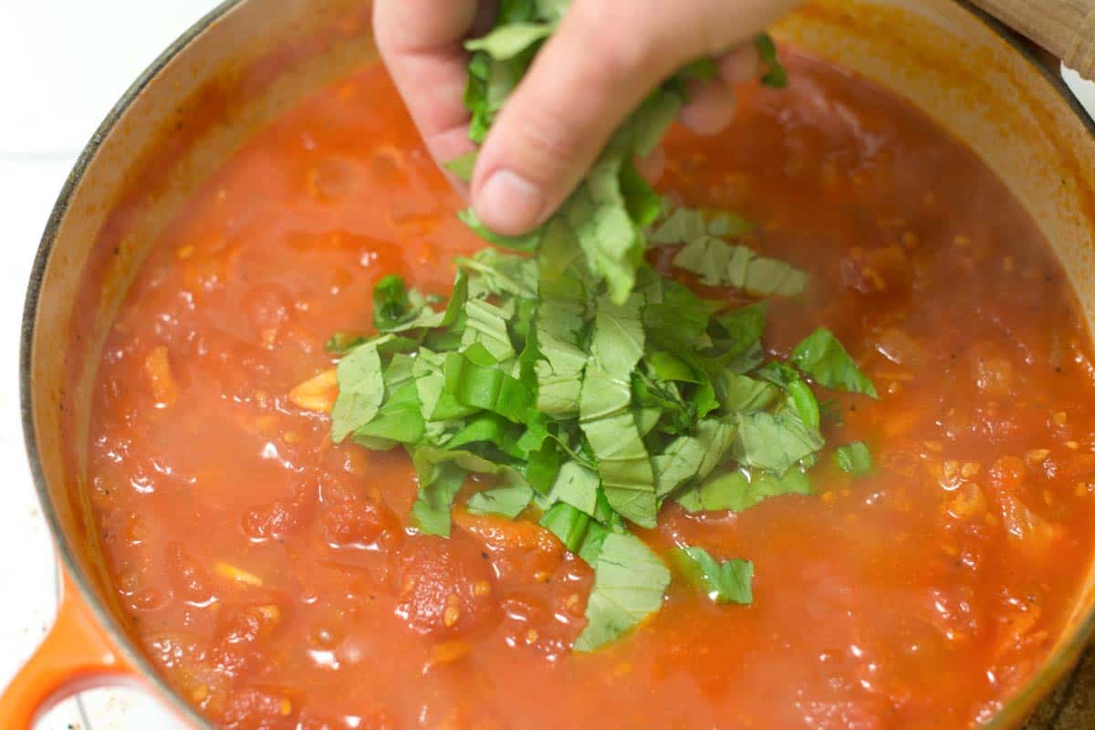 Adding fresh basil to homemade marinara.