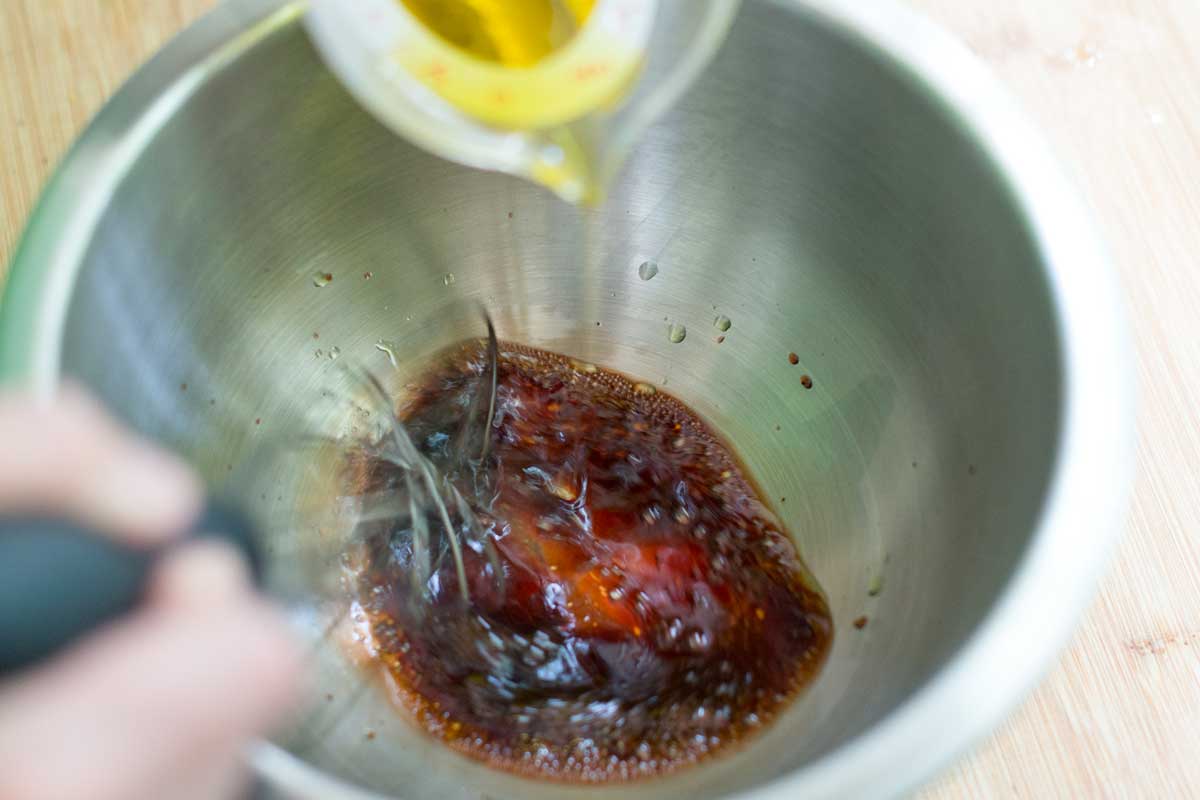 Slowly whisking oil into a bowl to make balsamic vinaigrette