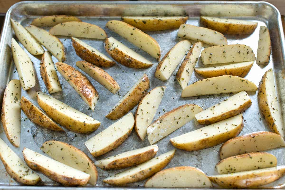 Seasoned potato wedges on a baking sheet ready to bake.