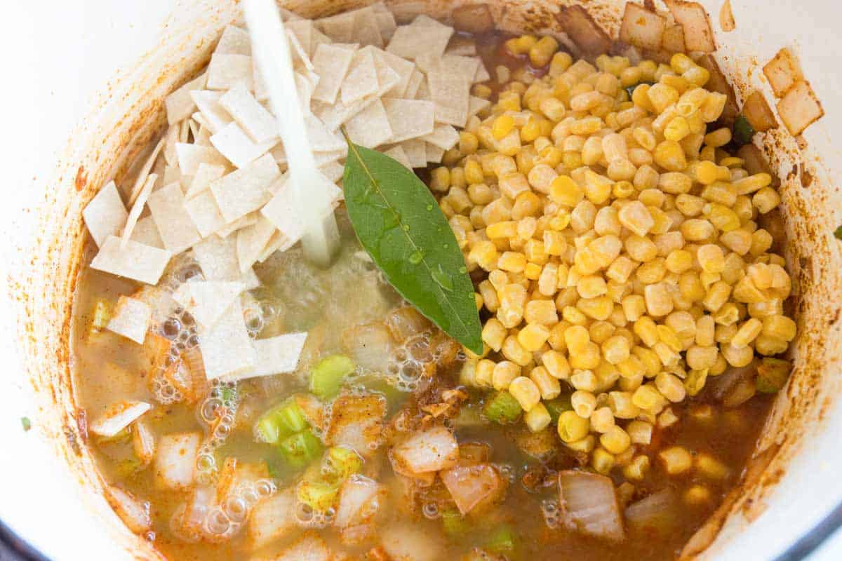 Adding the chicken stock, tortillas, and corn.
