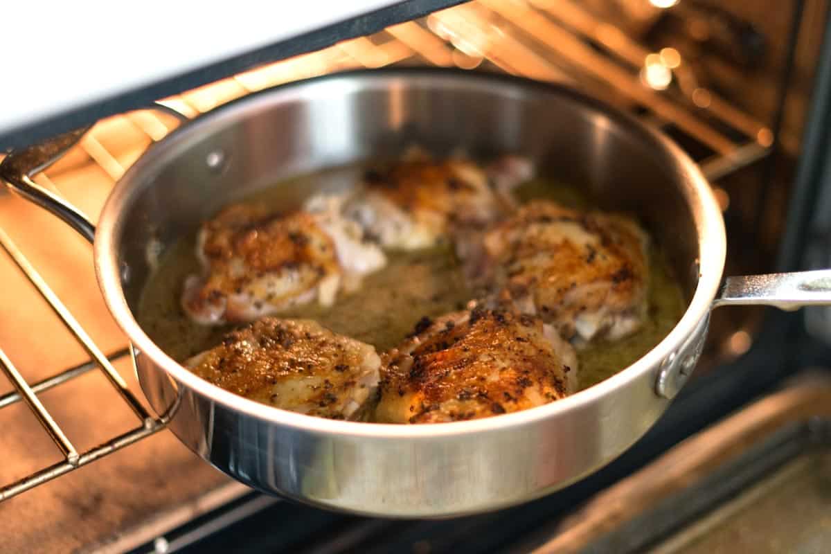 Placing a pan of lemon chicken thighs into the oven to finish cooking .