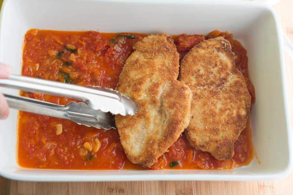 Adding crispy chicken to a baking dish with marinara sauce for chicken parmesan
