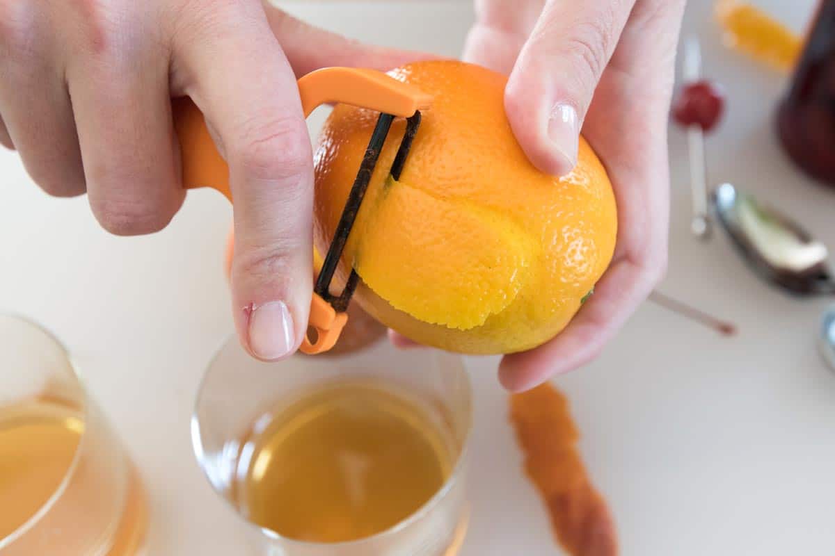 Old Fashioned Cocktail with Tips Peeling an orange over the glass to make an Old Fashioned cocktail