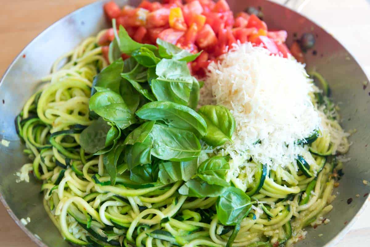 Adding tomatoes, basil, and cheese to zucchini noodles