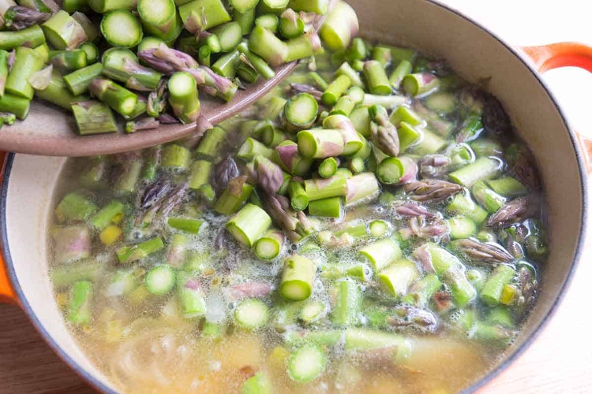 Adding chopped asparagus to the soup pot.