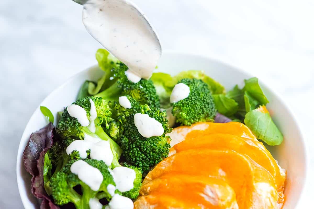 Assembling buffalo chicken rice bowls with rice, veggies, chicken, and buffalo sauce