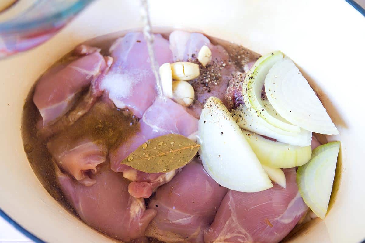 Simmering chicken thighs with water, onion, garlic, and spices to make shredded chicken