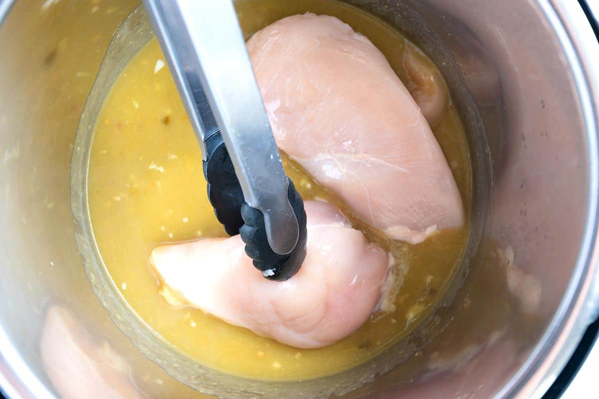 Placing chicken breasts into the Instant Pot with green enchilada sauce