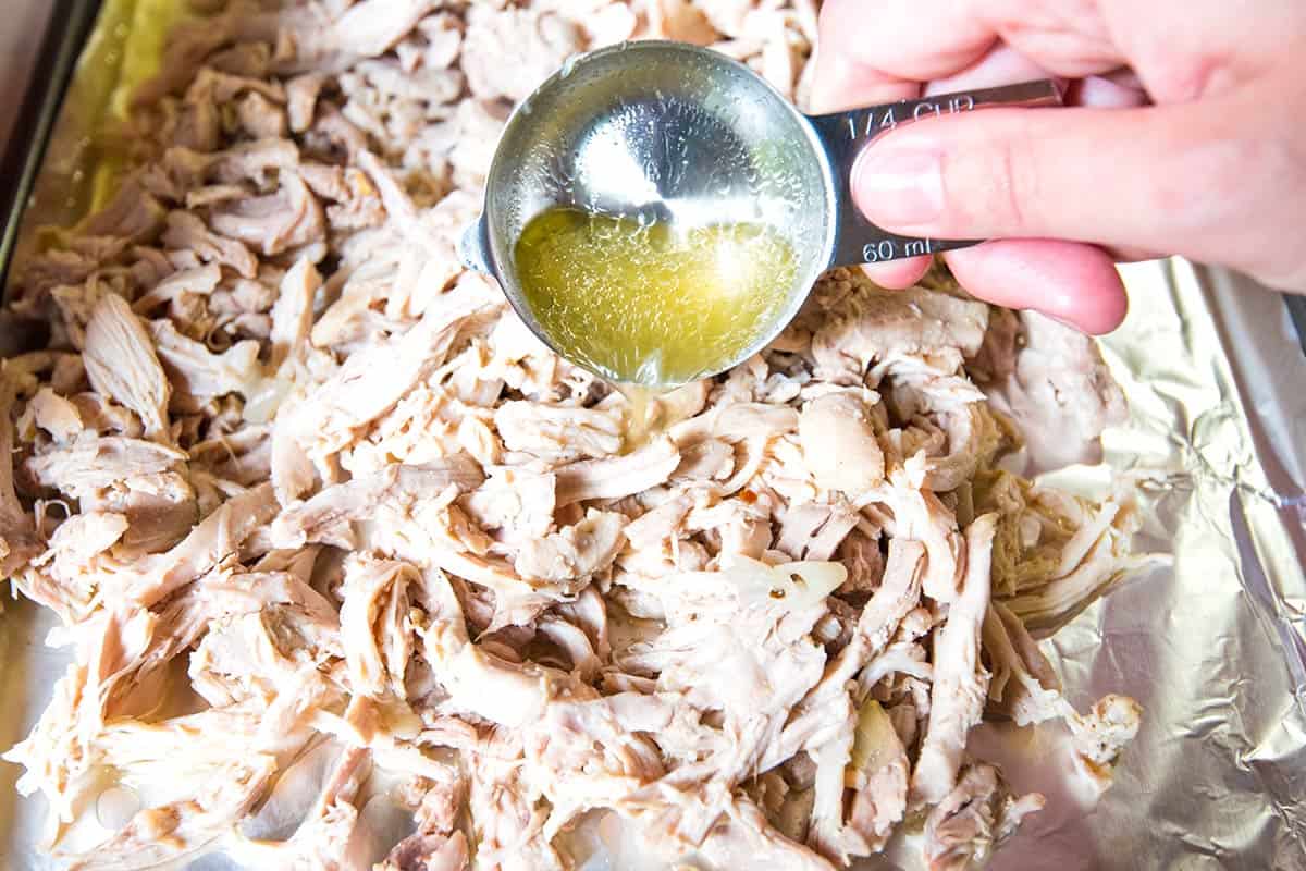 Spooning the cooking liquid over the shredded chicken for extra flavor