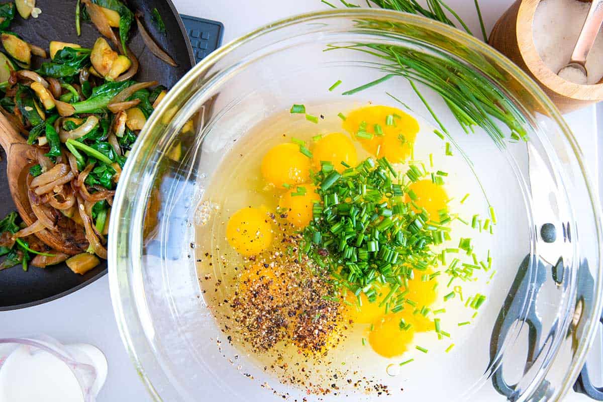 Eggs, veggies, and herbs in a bowl to make breakfast sandwiches.
