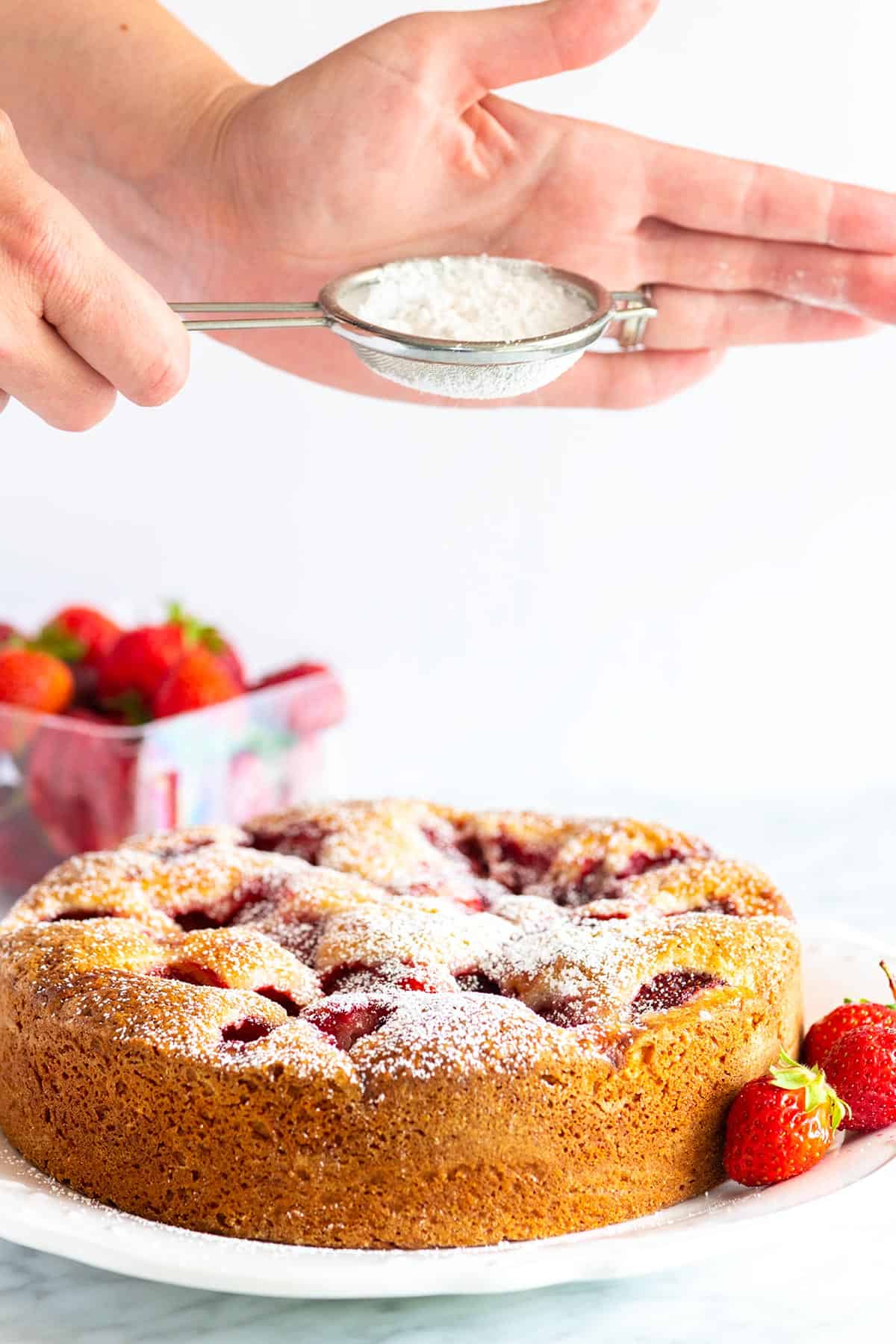 Stunning fresh strawberry cake recipe that’s extremely simple to make. The batter is made in one bowl! So easy. Dusting powdered sugar on top of strawberry cake