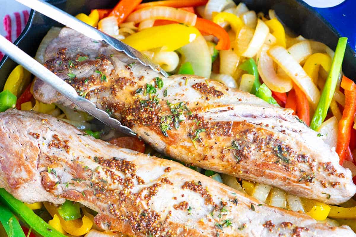 Setting seared tenderloins on top of a bed of peppers and onions