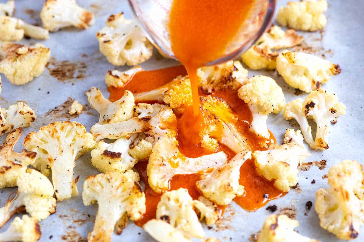 Cauliflower wings recipe step: Pouring buffalo sauce over roasted cauliflower