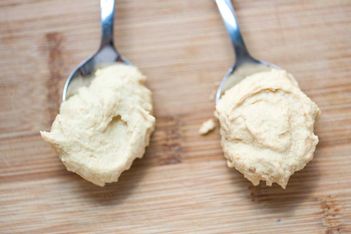 A photo showing the comparison of hummus made with peeled chickpeas on the left and skin-on chickpeas on the right.