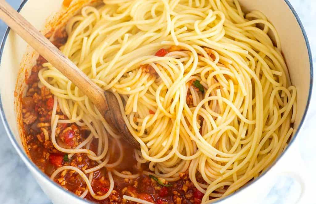 Stirring cooked spaghetti into sauce