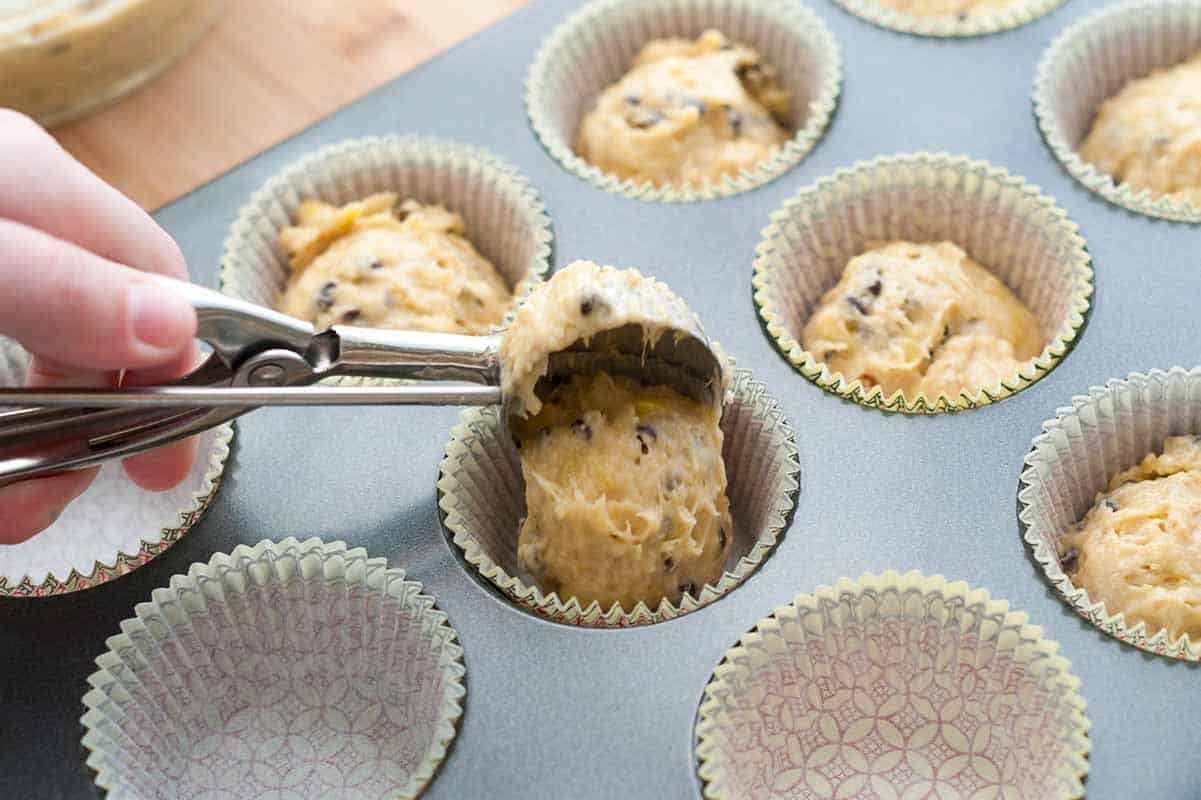Adding banana muffin batter to a muffin tin