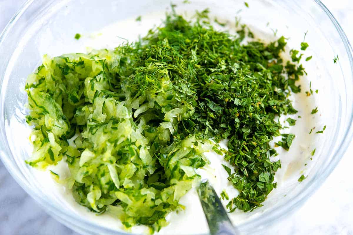 Stirring grated and squeezed cucumber and herbs into yogurt for tzatziki sauce
