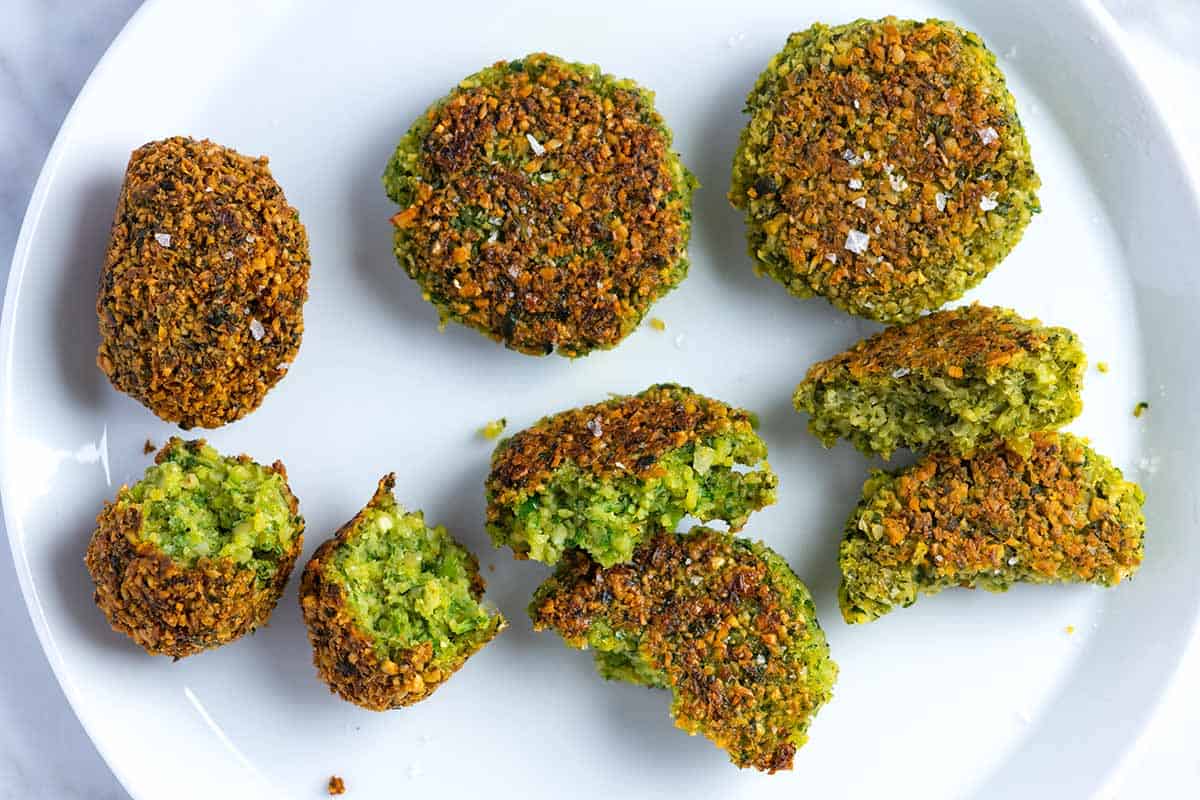 Three falafel on a plate. The one on the left is deep fried which looks golden brown and tender inside. The middle is pan-fried, which is less crispy on the outside, and the one on the right is baked, which is less crispy and less green inside compared to the others.
