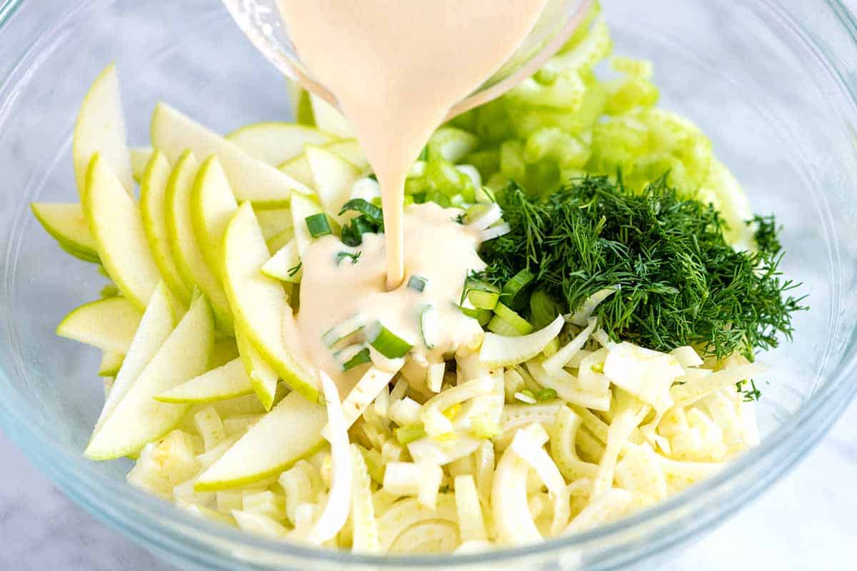 Adding dressing to apples, celery, and fennel to make salad