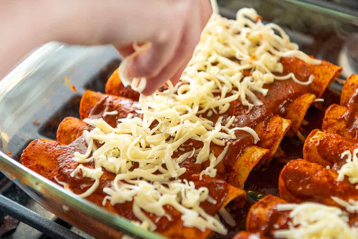 Adding cheese to rolled chicken enchiladas before baking