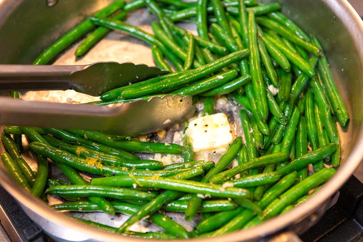 Adding garlic and butter to green beans in pan