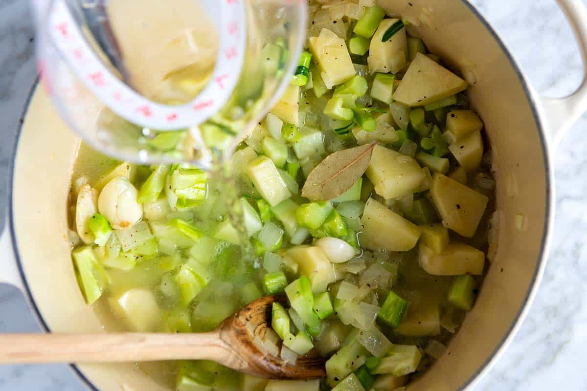 Adding broth to the pot with potatoes, broccoli, and onions.
