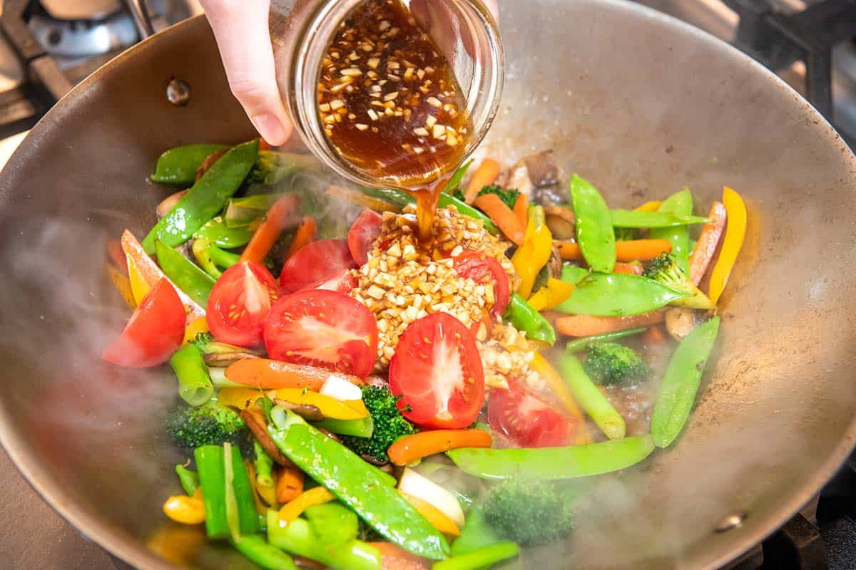 Pouring stir fry sauce into a wok with vegetables