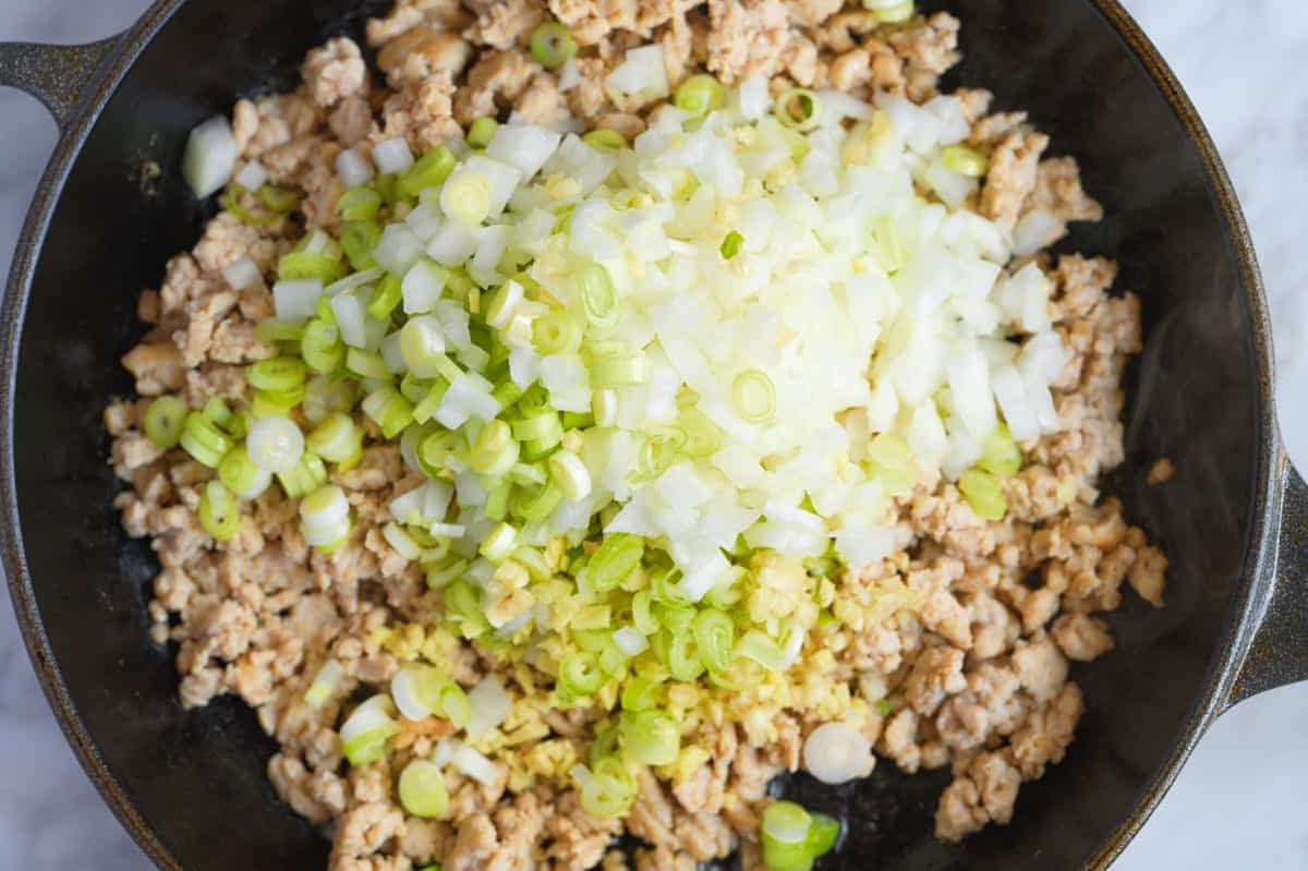 Stirring aromatics like garlic, ginger and onion into ground chicken for Asian chicken lettuce wraps