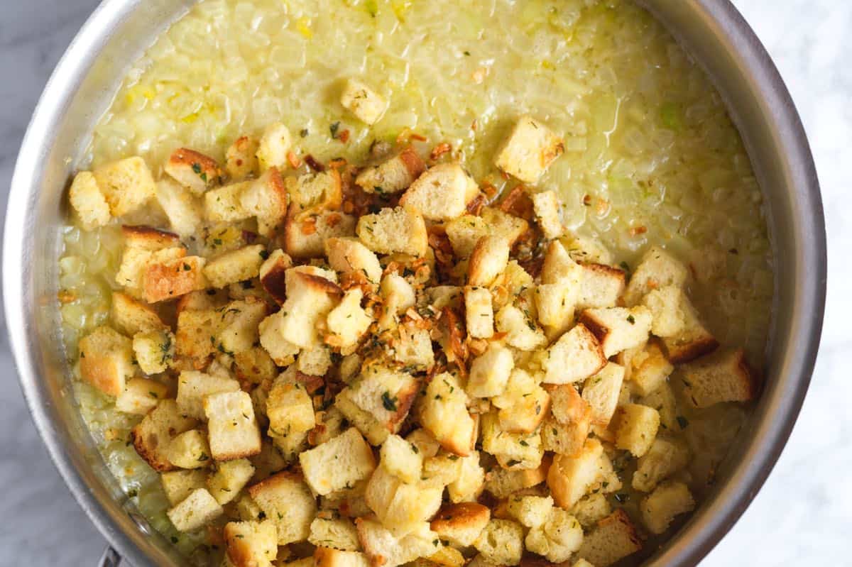 Toasted bread in a pan with broth, onions, and herbs for homemade stuffing.