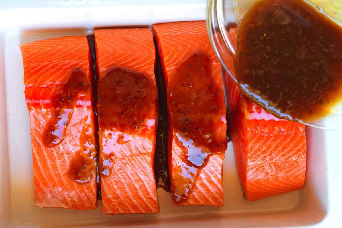 Pouring the salmon glaze over salmon fillets in a baking dish