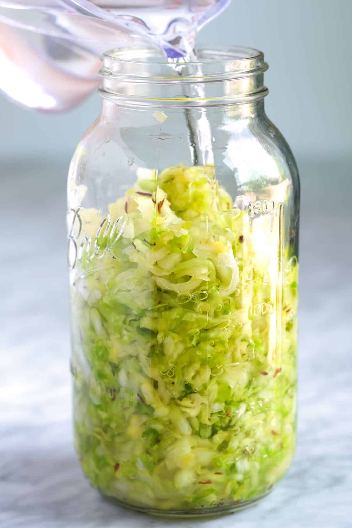 Pouring a 2% salt brine into a jar with salted cabbage