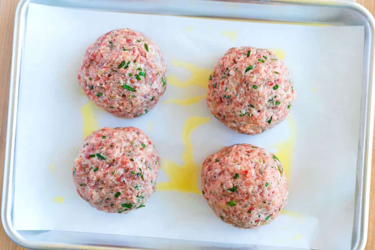 Four big meatballs on a baking sheet ready to go into the oven.