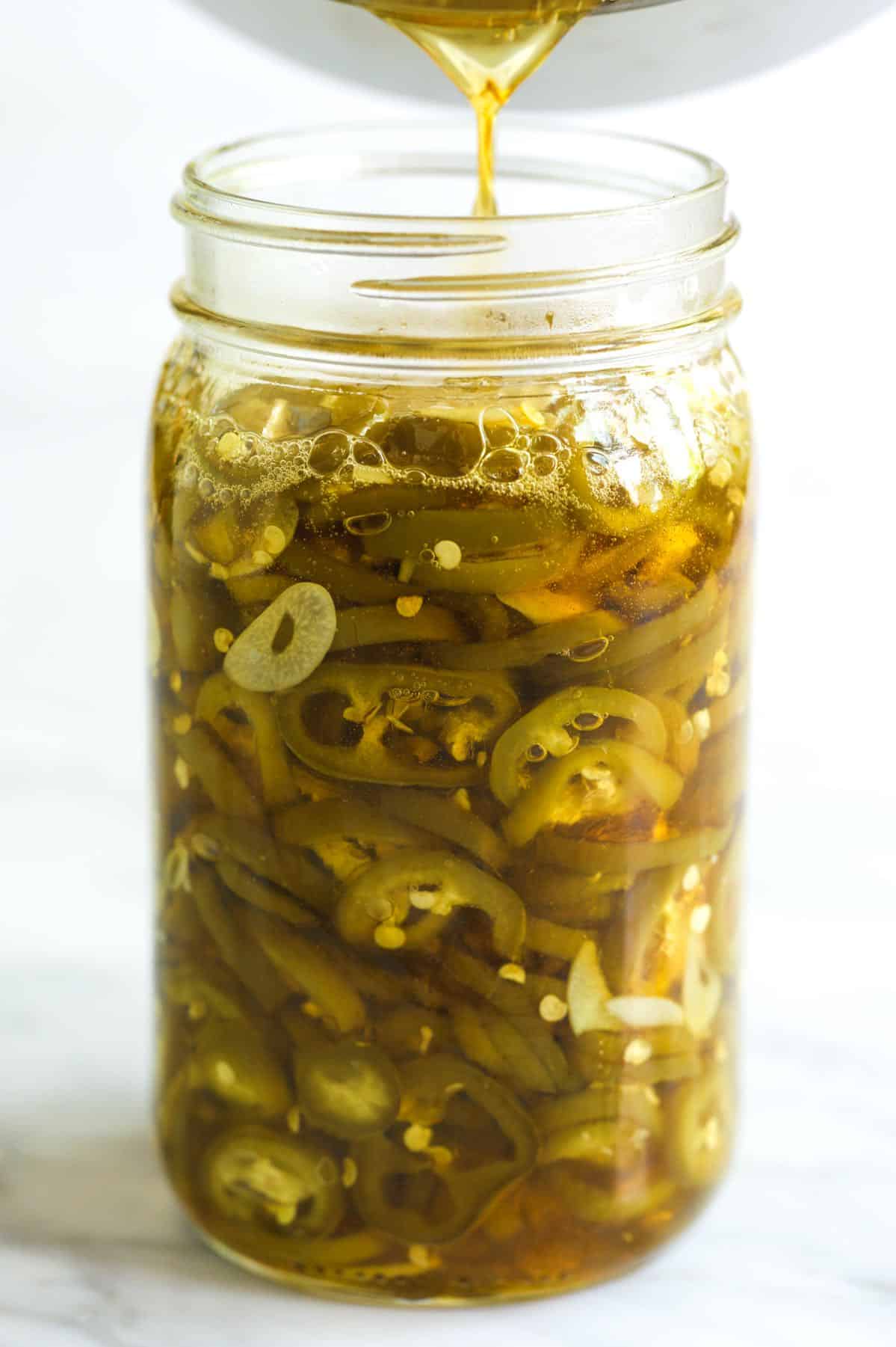 Pouring a sugar syrup into a jar with jalapeños and garlic.