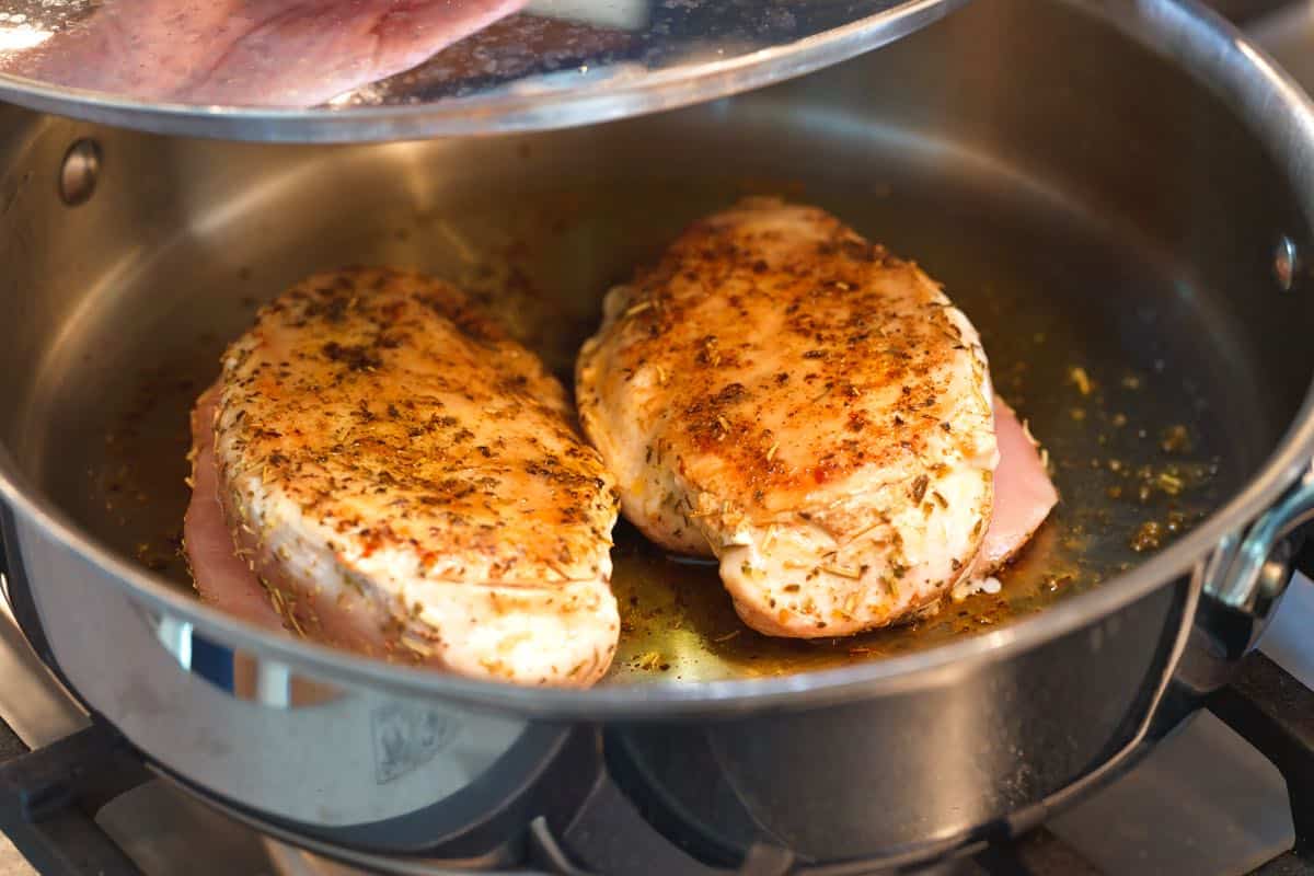 Cooking seasoned chicken breasts in a skillet.