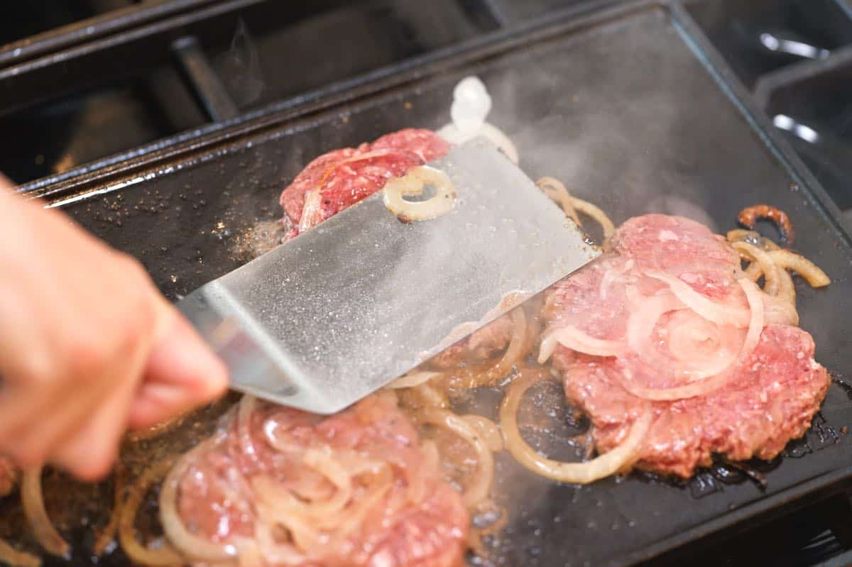 Pressing out ground beef into smash burgers using a stiff spatula.
