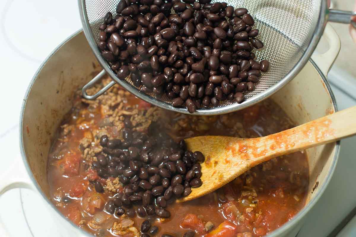Adding the black beans to the pot with ground turkey, spices, and tomatoes