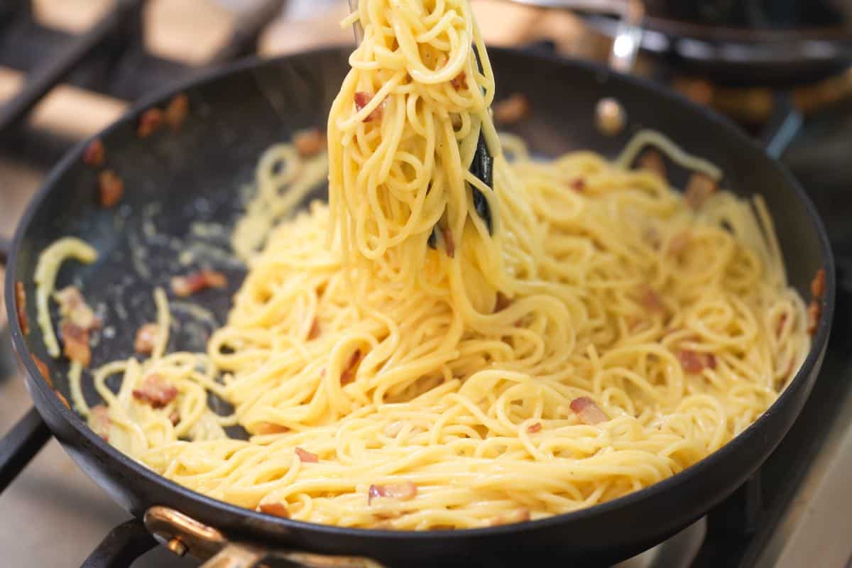 Tossing the egg and cheese mixture with pasta in a skillet