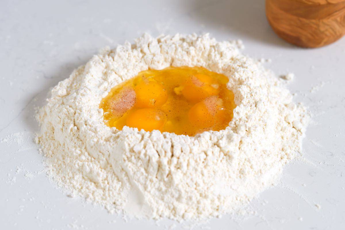 Flour with eggs, salt, and olive oil in a well in the middle on the counter for fresh pasta