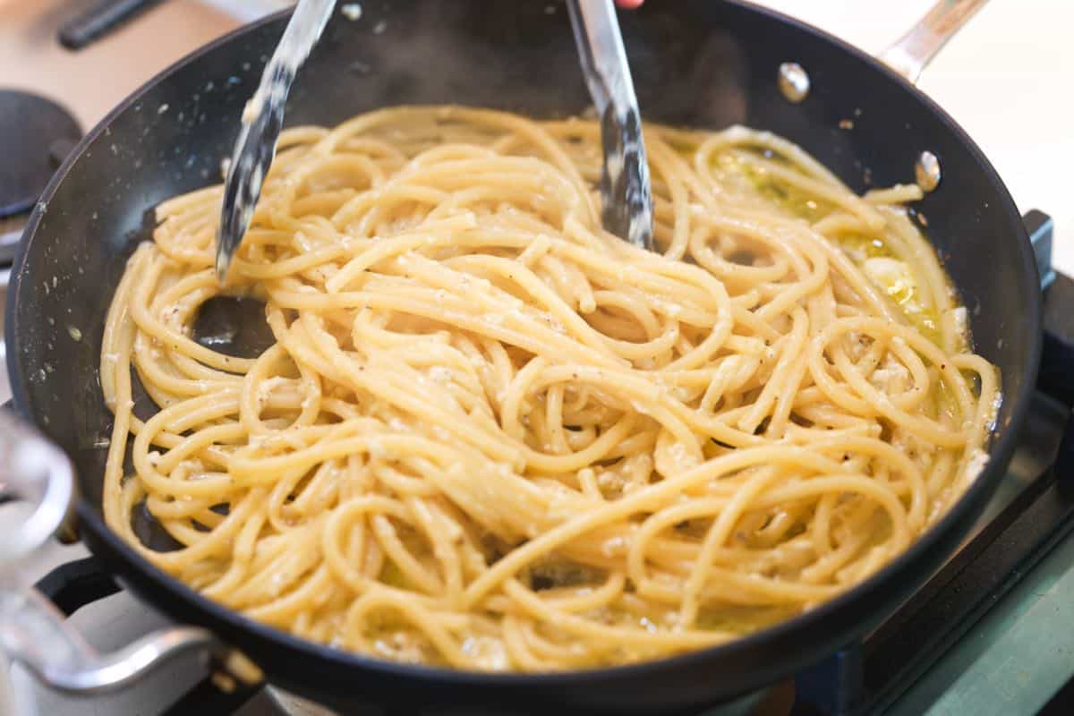 Tossing bucatini in a skillet with pecorino cheese, black pepper, and pasta water