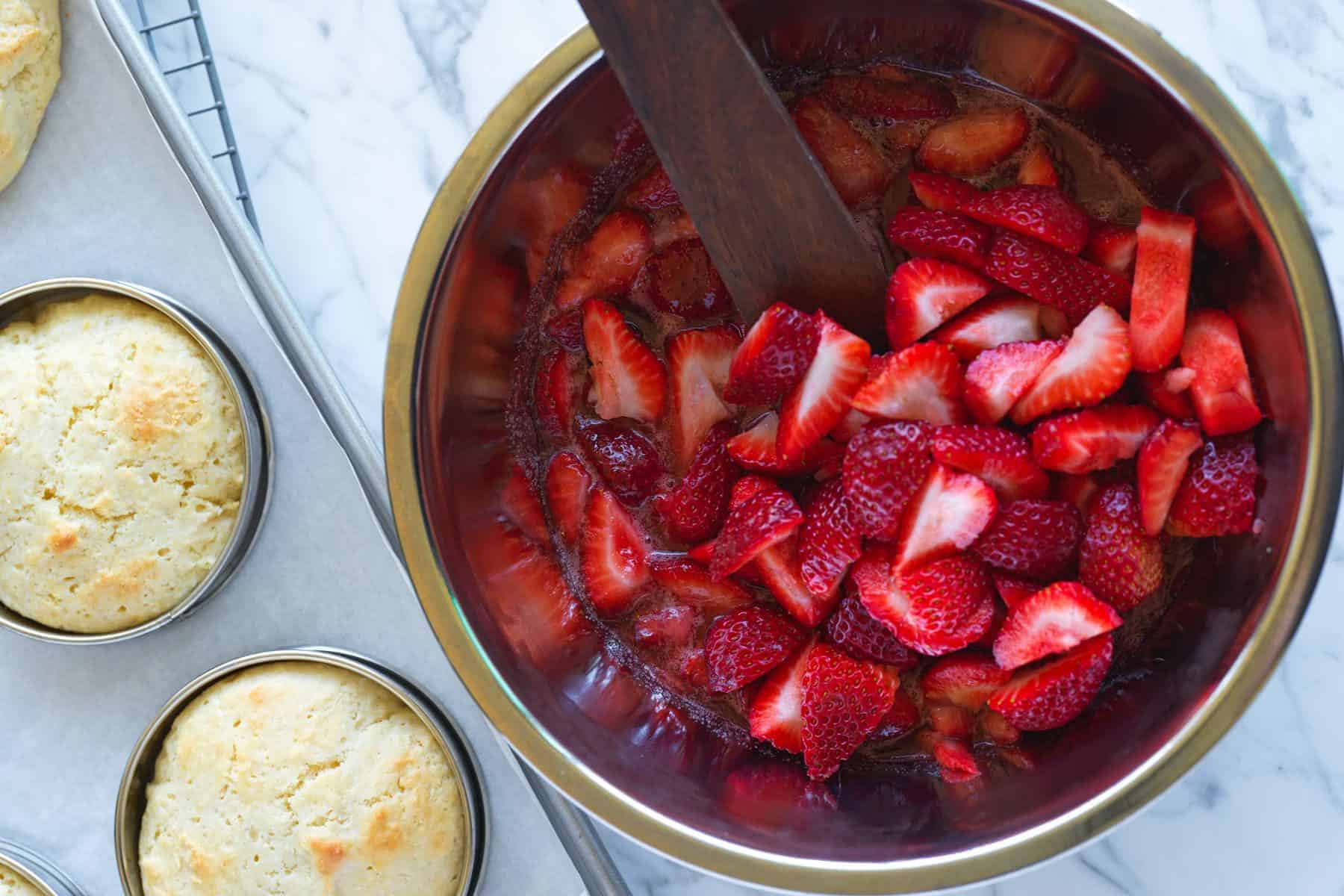 Fresh strawberries in homemade strawberry syrup and baked biscuits ready to assemble strawberry shortcake