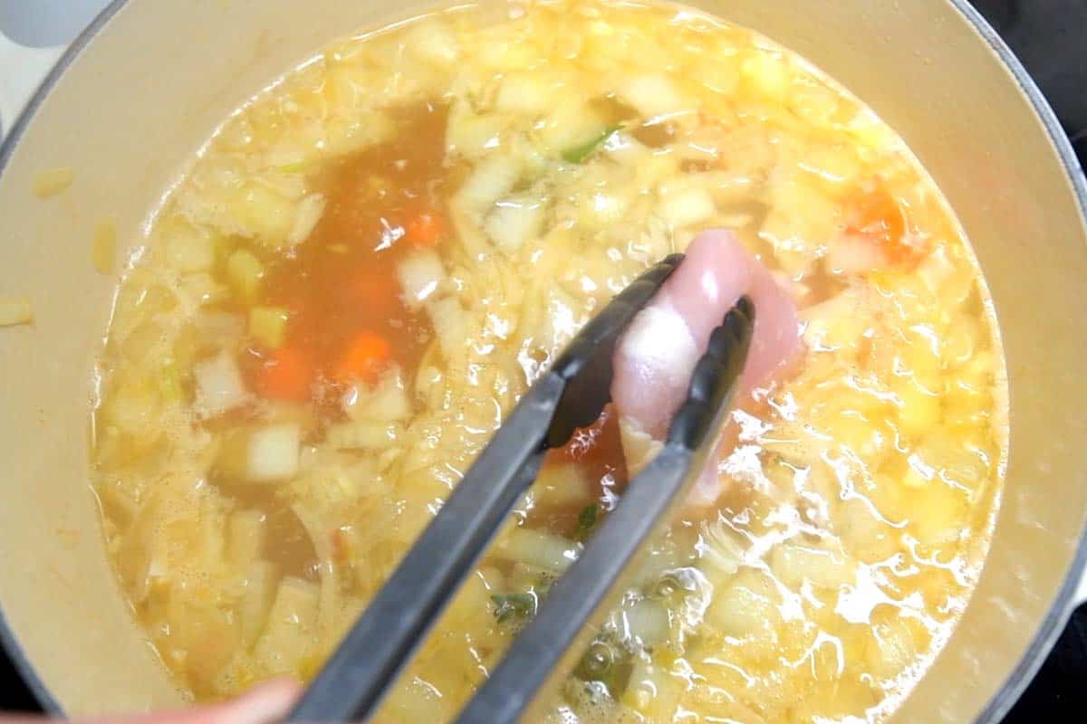 Adding chicken thighs to broth for chicken noodle soup