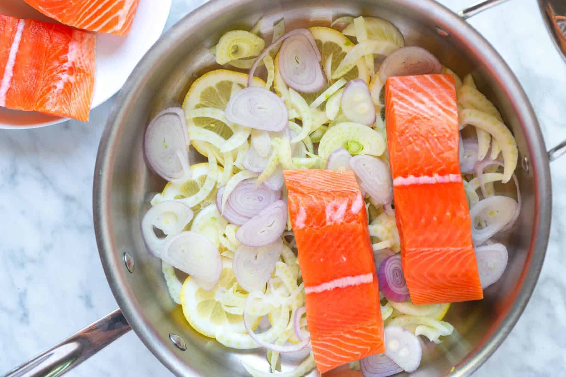 Skillet with lemon slices, shallot, fennel and salmon fillets almost ready for poaching