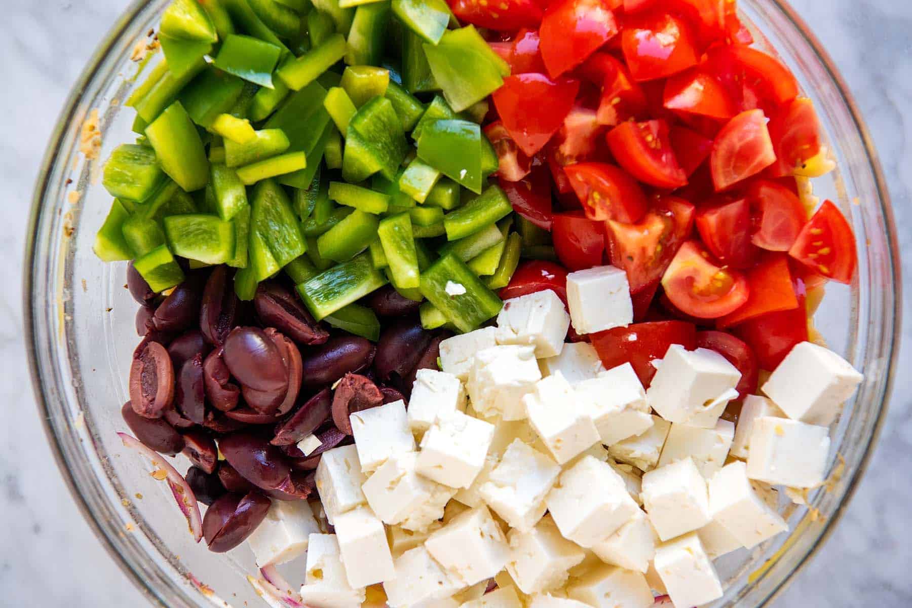 Greek pasta salad ingredients in a bowl ready to be tossed