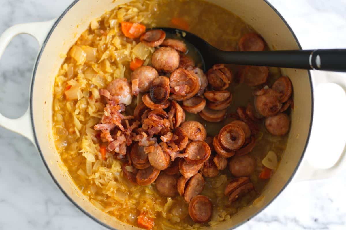 Stirring cooked kielbasa and bacon back into the sauerkraut soup before serving